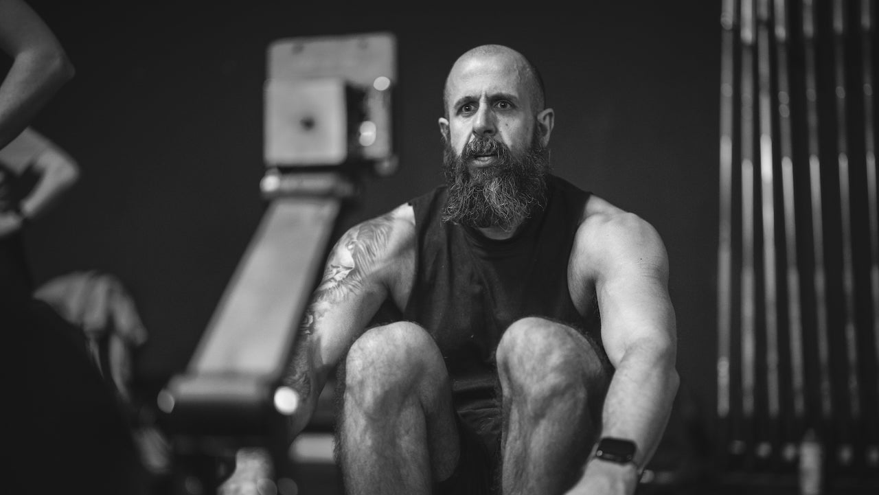 Man with a beard and tattoos using a rowing machine in a gym setting.